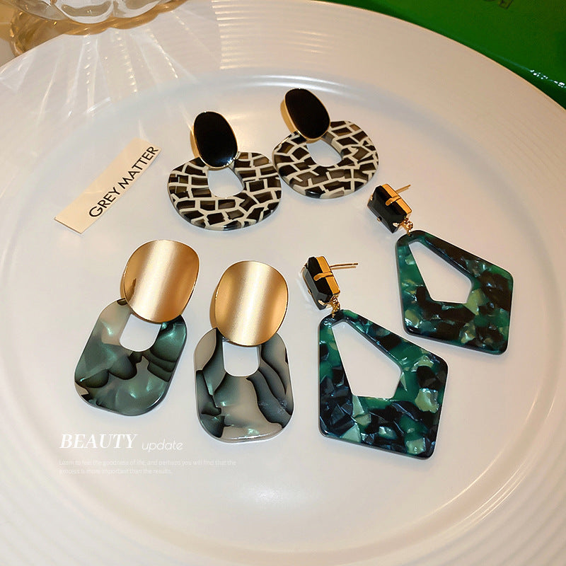 Colorful geometric statement earrings with gold and marbled resin design on a white plate