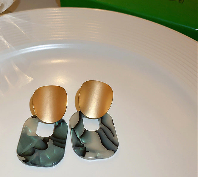 Gold and marble green acrylic statement earrings on a white plate