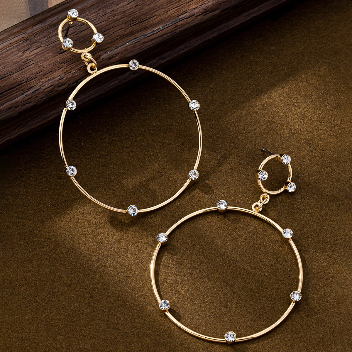 Gold hoop earrings with clear crystal accents on brown background