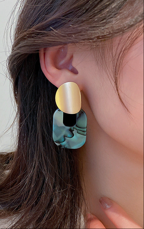 Woman wearing modern geometric gold and green statement earring, close-up view