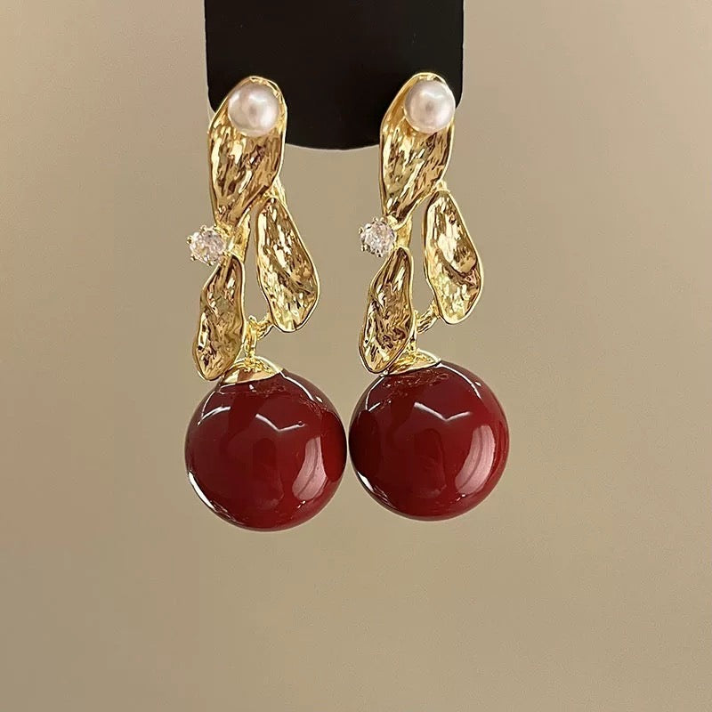 Gold-toned earrings with pearl, crystal, and large red stone dangle accents