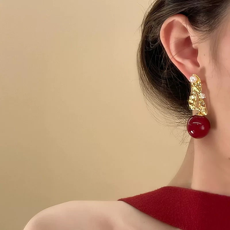 Gold textured earring with pearl and red stone drop, worn by woman with updo