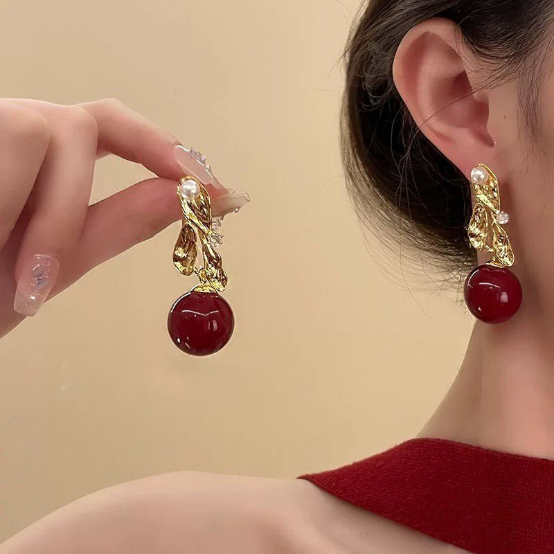 Woman wearing gold-tone drop earrings with red stone beads and pearl detailing