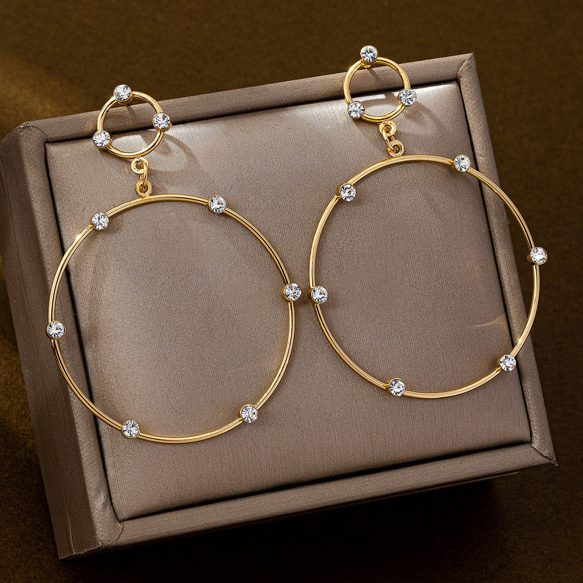 Gold hoop earrings with sparkling crystal accents displayed on a brown jewelry box