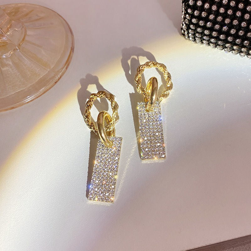 Gold rectangular crystal drop earrings on a white surface, sparkling under light