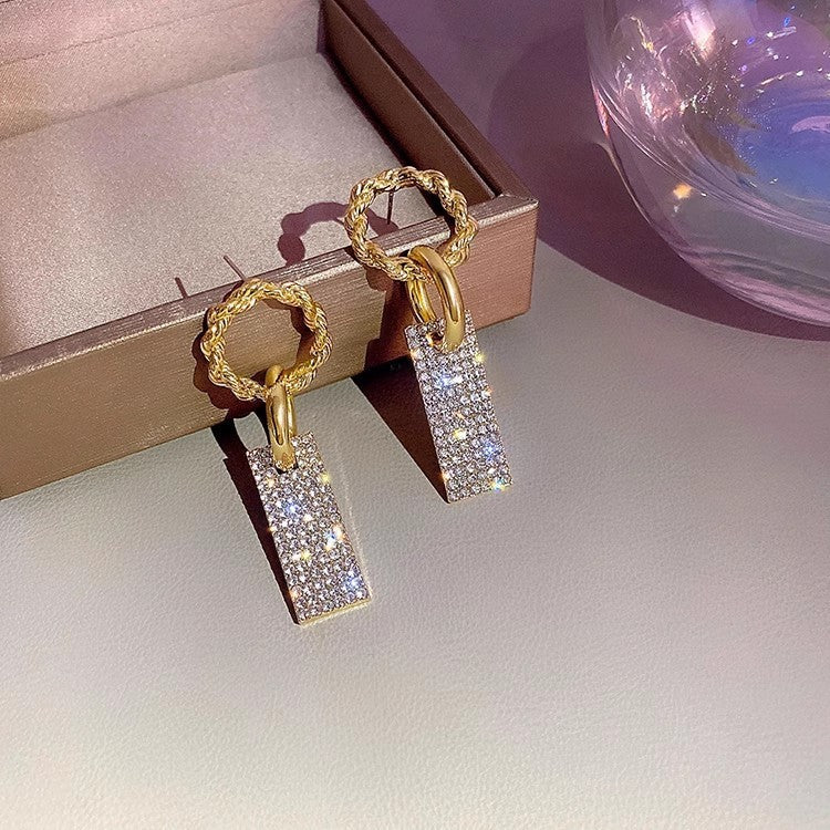 Gold rectangular drop earrings with sparkling crystals on a jewelry box