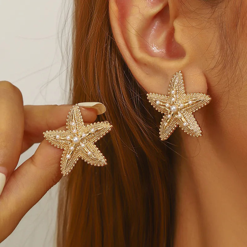 Gold starfish earrings with pearl accents on ear and hand, tropical beach style jewelry