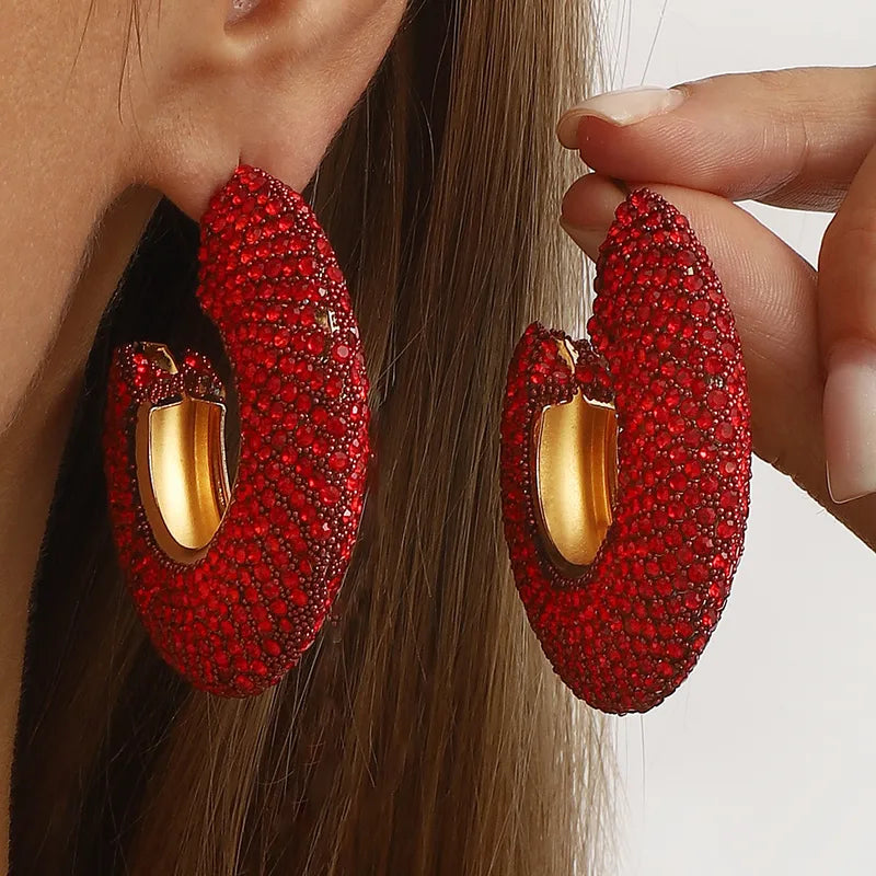 Elegant red crystal C-shaped hoop earrings with gold-tone interior on a woman's ear