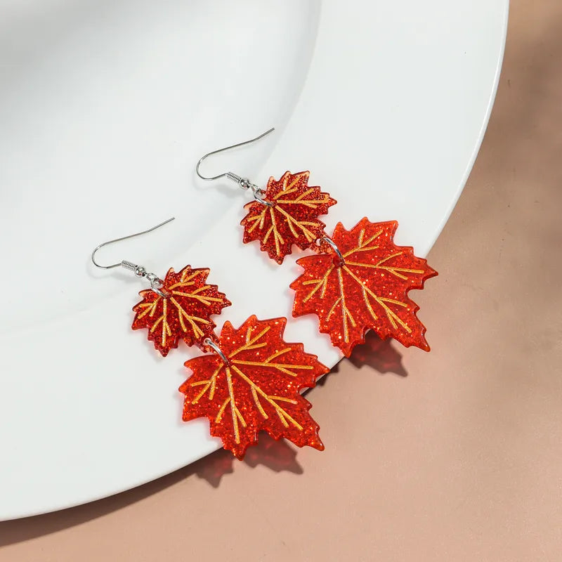 Glittery red maple leaf dangle earrings on a white plate, statement jewelry design